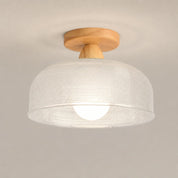 White woven dome ceiling light with wooden mount and glowing bulb on a neutral background.