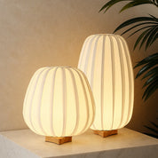 Two warm glowing ribbed table lamps with wooden bases sit on a light marble surface.