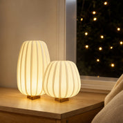 Two warm glowing ribbed fabric table lamps with small wooden bases on a bedside shelf.