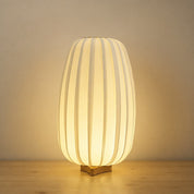 Glowing ribbed cream table lamp with a small wooden base on a neutral tabletop.