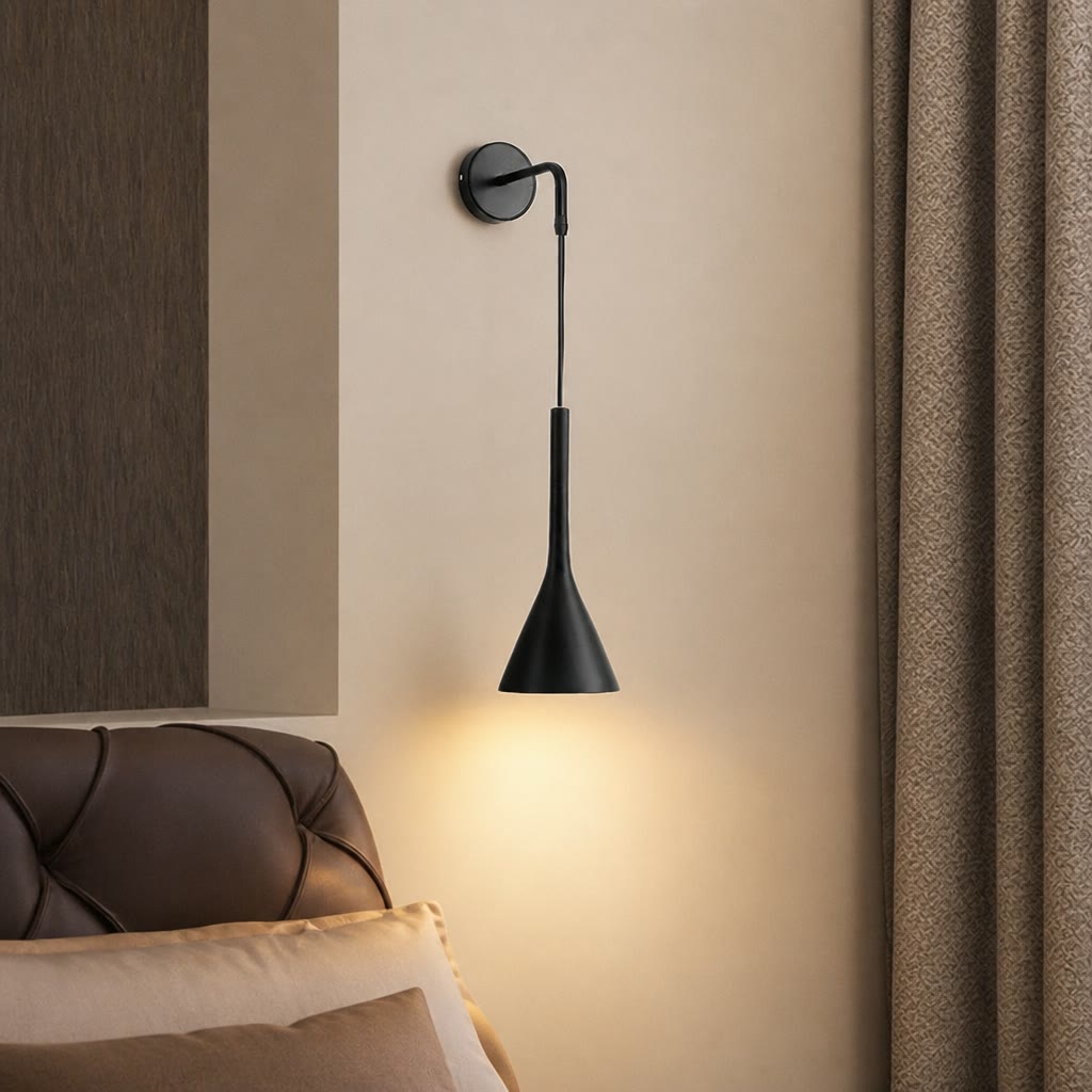 Black cone wall sconce glowing warmly beside a tufted leather headboard.