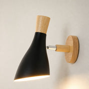 Black and wood wall sconce with cone shade lit against a plain light wall.