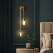 Brass wall sconce with two glowing tube lights above a bedside table.