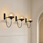 Three glowing glass globe wall sconces with black looped cords and brass accents on a white wall.