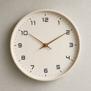 Beige wall clock with black numerals and slim wooden hands on a light wall.