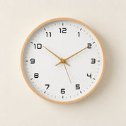 Round wood-rimmed wall clock with black numerals and gold hands on a pale wall.
