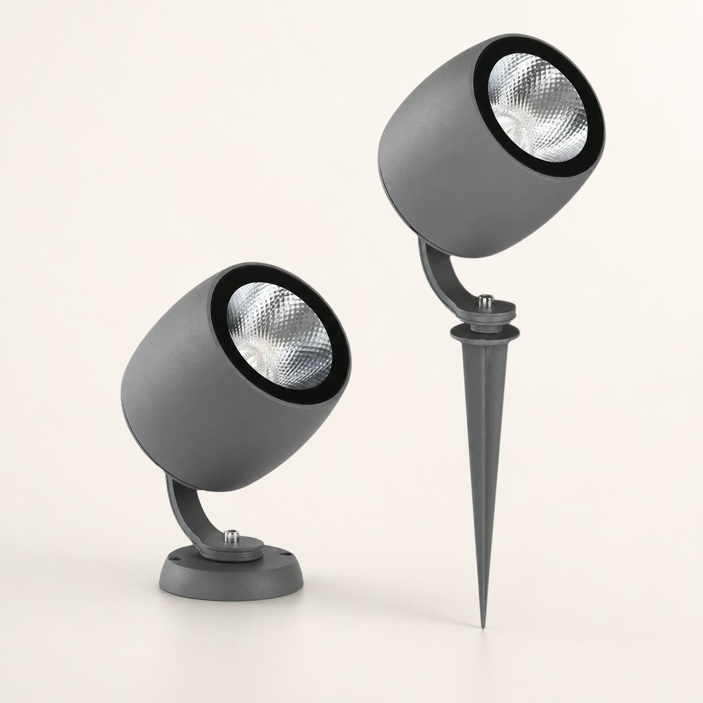 Two gray cylindrical outdoor spotlights with black rims and silver reflectors, one on a base and one on a ground spike.