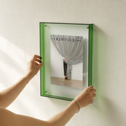 Green transparent wall frame displaying The Kinfolk Home book, held by two hands.