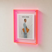 Pink acrylic wall frame displaying a CÉLINE fashion poster on a pale wall.