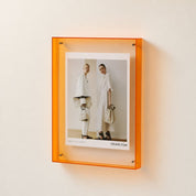 Orange translucent wall-mounted poster frame displaying a Celine fashion print.