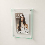 Transparent green-edged wall display frame holding a fashion magazine cover.
