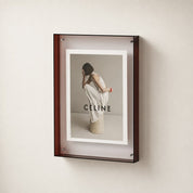 Wall-mounted reddish-brown display frame holding a CÉLINE fashion poster on a pale wall.