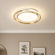 Gold ring ceiling light glowing warmly above framed wall art in a neutral room.