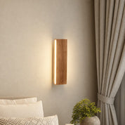 Wooden wall sconce with warm vertical light mounted beside a bed and curtains.