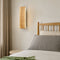 Rectangular wooden wall sconce glowing beside a neutral bed.