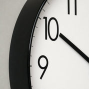 Close-up of a black-framed analog wall clock with a white face and bold black numerals.