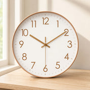 White wall clock with bronze numerals and hands on a light wooden surface.