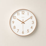 Round white wall clock with rose gold rim, numerals, and hands on a pale neutral background.