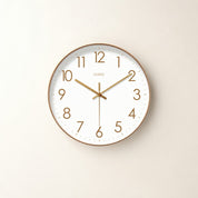 Round white wall clock with gold numerals and hands on a pale neutral background.