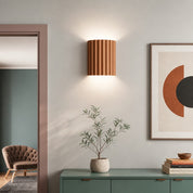 Fluted wooden wall sconce above a green console with a small potted plant.
