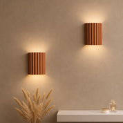 Two ribbed terracotta wall sconces glowing warmly above a white console with dried wheat.
