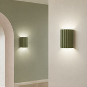 Two olive green ribbed cylindrical wall sconces casting soft up-and-down light.