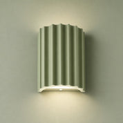 Sage green fluted wall lamp with a white base casting a soft downward glow.