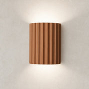 Ribbed terracotta cylindrical wall sconce casting soft light on a neutral wall.