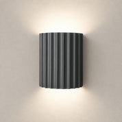 Dark ribbed cylindrical wall sconce emitting warm light above and below.