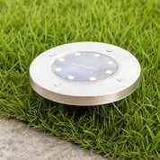Round stainless steel solar garden light with solar panel set in grass.