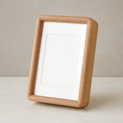 Light wooden picture frame with a blank white mat leaning on a pale tabletop.