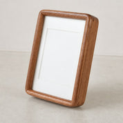 Rounded wooden picture frame leaning on a pale tabletop with a blank white mat inside.
