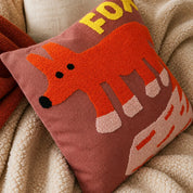 Dusty rose cushion with a tufted orange fox design on a cozy neutral blanket.