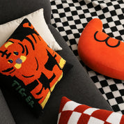 Tiger cushion and orange heart pillow on a dark sofa with a checkered rug.