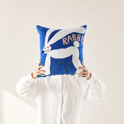 Blue square rabbit cushion held by a person in a white shirt.