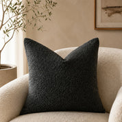 Black textured square pillow on a cream boucle armchair in a neutral living room.