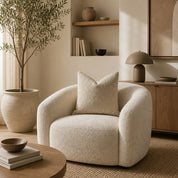 Cream boucle armchair with rounded arms and a matching textured pillow in a warm neutral living room.