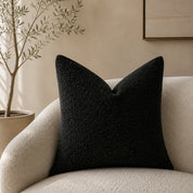Black textured square throw pillow on a cream boucle armchair in a neutral living room.
