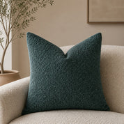 Dark teal textured throw pillow on a cream boucle armchair in a warm neutral room.
