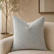 Light gray textured square throw pillow on a cream boucle chair.