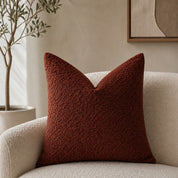 Rust red textured square pillow on a cream boucle armchair in a warm neutral room.