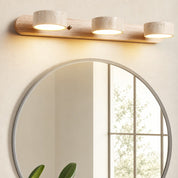 Three-light wood and stone vanity fixture glowing above a round mirror.