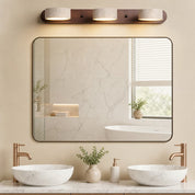 Three-light vanity fixture with stone shades above a bathroom mirror and marble sinks.