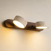 Two-light wall sconce with wood backplate and cream stone shades glowing warmly.