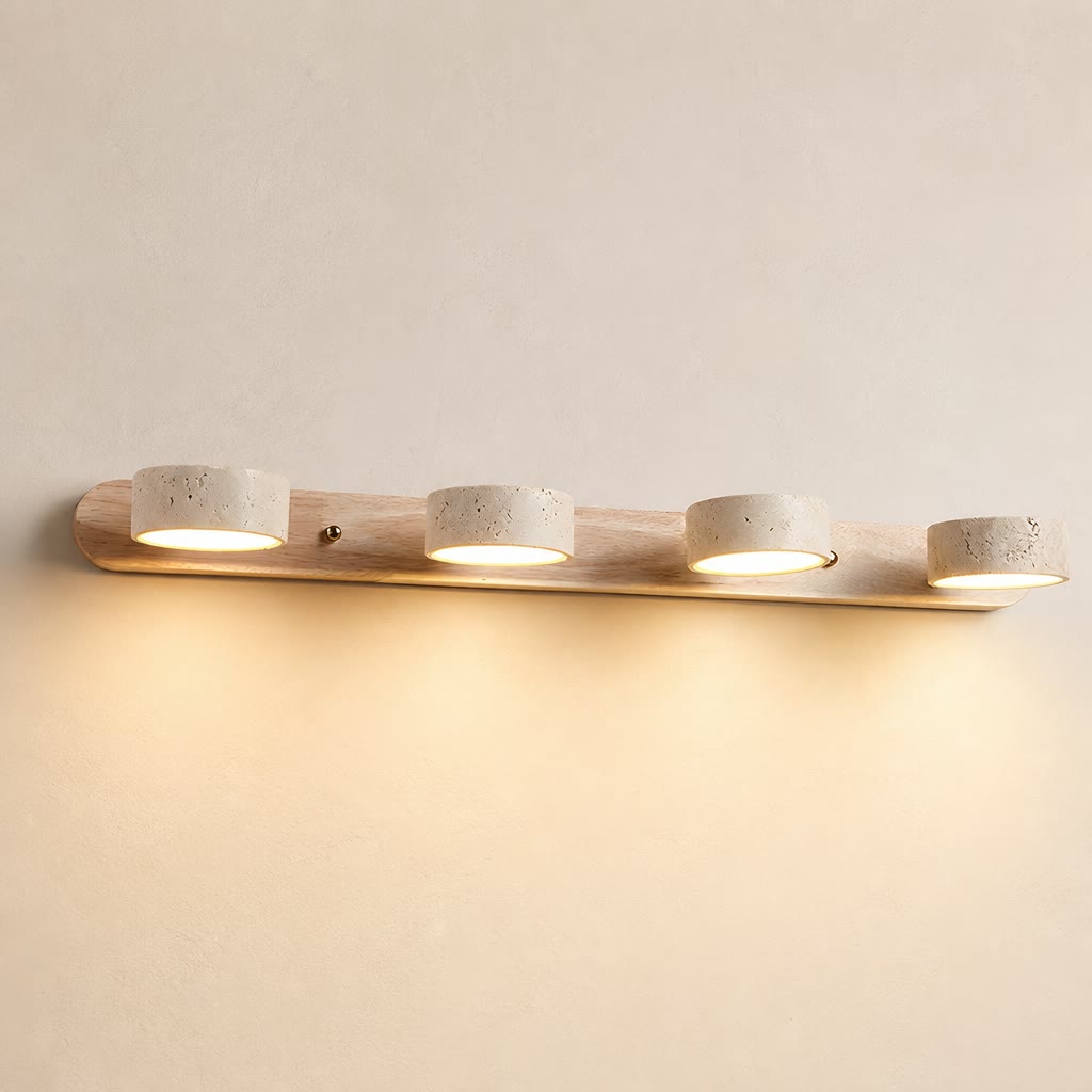 Four-light wooden vanity fixture with stone-textured round shades glowing warm on a pale wall.