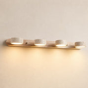 Four-light wooden vanity fixture with stone-textured round shades glowing warm on a pale wall.