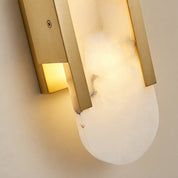 Brushed gold wall sconce with glowing alabaster shade mounted on a neutral wall.
