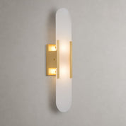 Frosted vertical wall sconce with warm brass accents and glowing light.