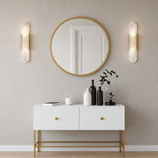 White two-drawer console with gold accents, round mirror, wall sconces, and decorative vases.