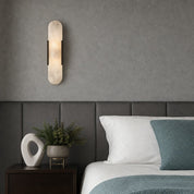 Vertical frosted wall sconce above a bed with gray headboard and teal bedding.